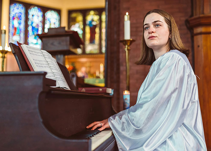 Woman in choir robe playing piano in church setting, embodying a cringe-worthy biblical experience.