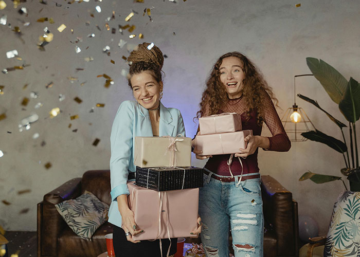 Two smiling women holding gifts amid confetti at a joyful celebration.