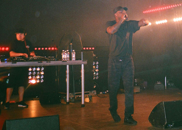 Performer on stage with a DJ in the background, vibrant lights create a dramatic atmosphere.