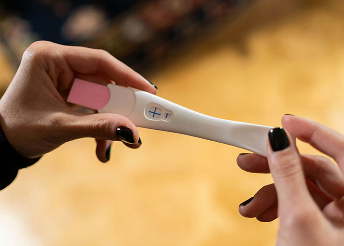 Person holding a pregnancy test showing a positive result, symbolizing a cringe-worthy experience.