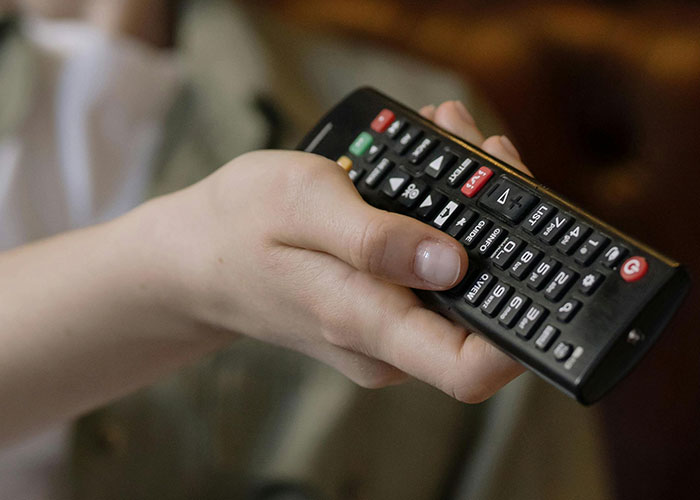 Hand holding a black remote control, symbolizing a common experience that might cause discomfort or cringe.