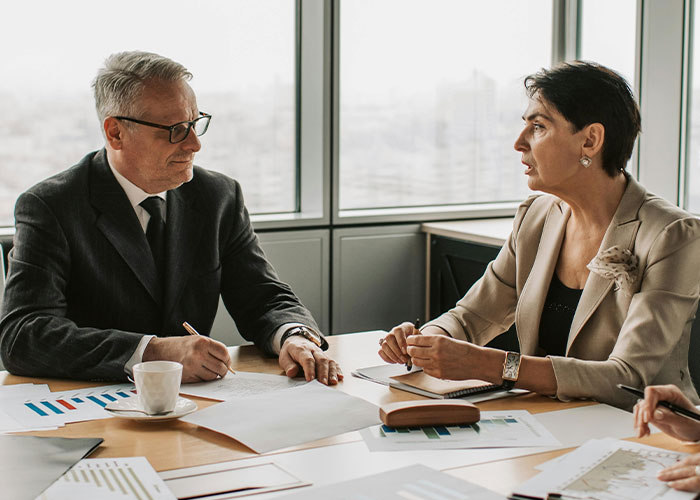 Business meeting with two people discussing documents at a conference table, near large windows.