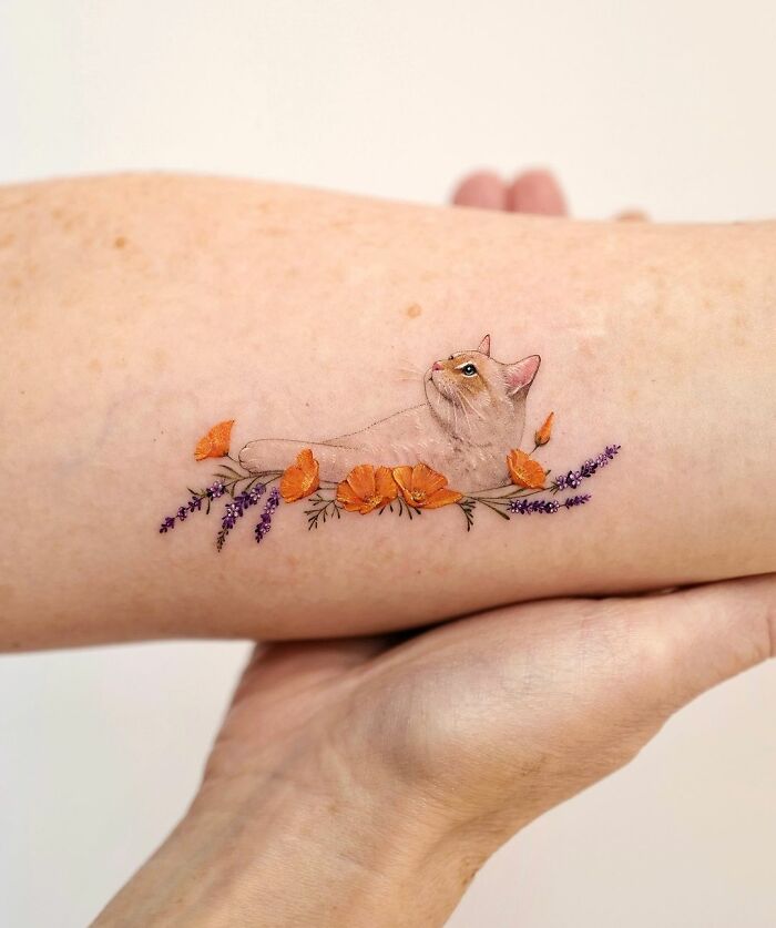 Cute pet portrait tattoo of a cat adorned with orange and purple flowers on an arm.