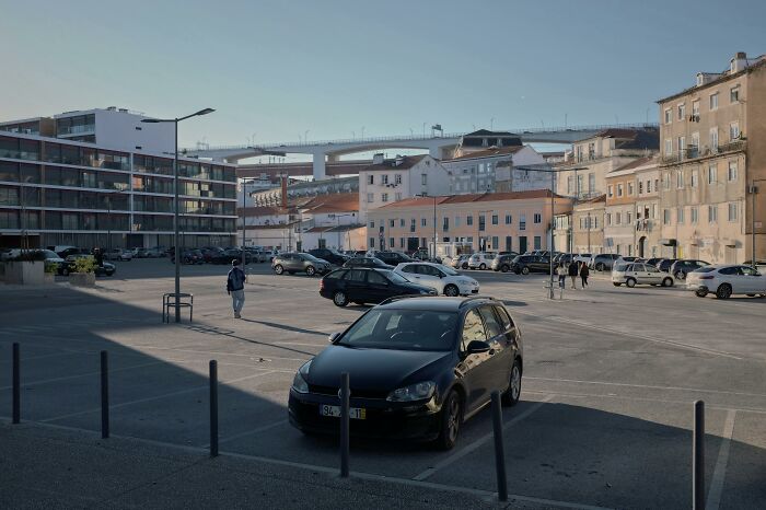 Black car parked in a mostly empty lot near residential buildings on a sunny day, showcasing frugal wins and saving money.