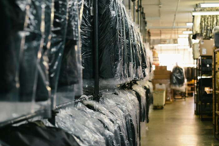 Clothing items covered in plastic bags hanging in a warehouse aisle, illustrating frugal wins and saving money.