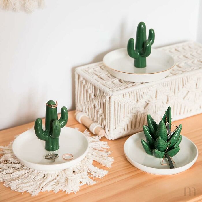 Green cactus jewelry holders displayed on white trays and a woven box on a wooden surface, showcasing random genius items.