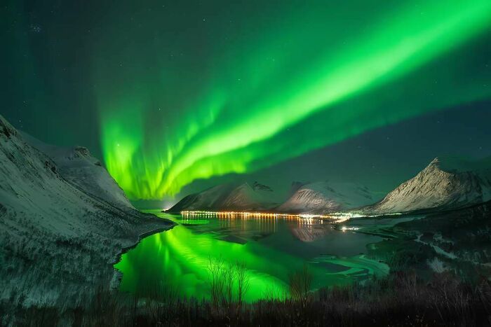 Aurora borealis lighting up the night sky over snowy mountains and a reflective lake in a breathtaking landscape photo.