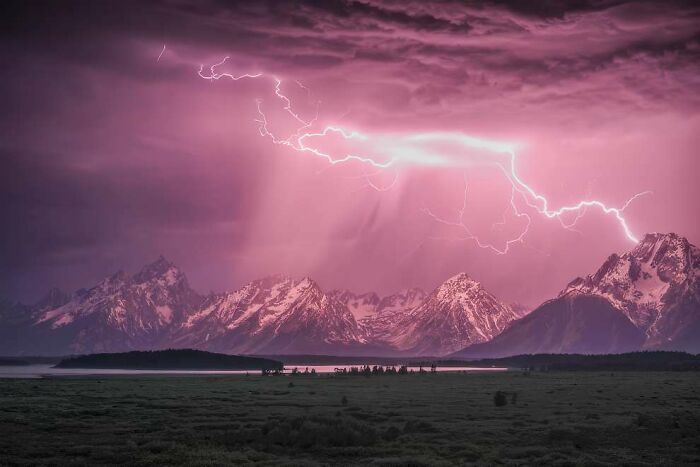 Lightning striking over snow-capped mountains during a stormy purple sky, showcasing breathtaking landscape photography.