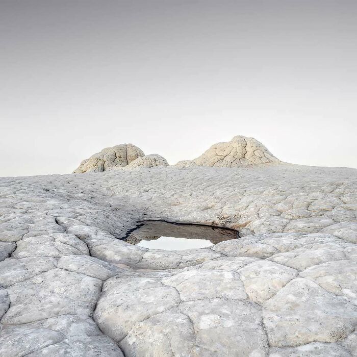 Breathtaking landscape photo of cracked pale rock formations with a small reflective water pool under an overcast sky.
