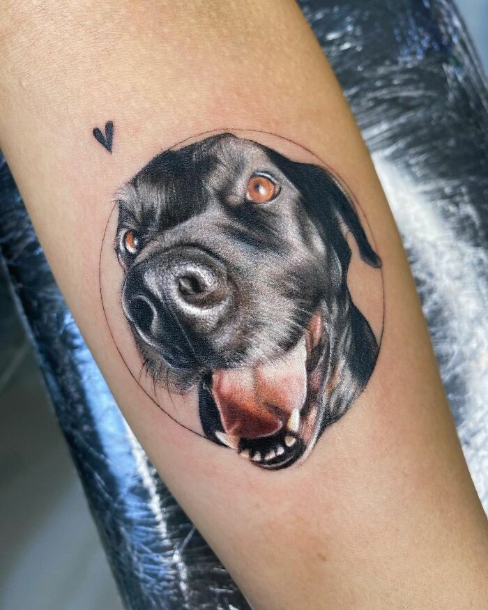 Cute pet portrait tattoo of a black dog with tongue out and a small heart design.