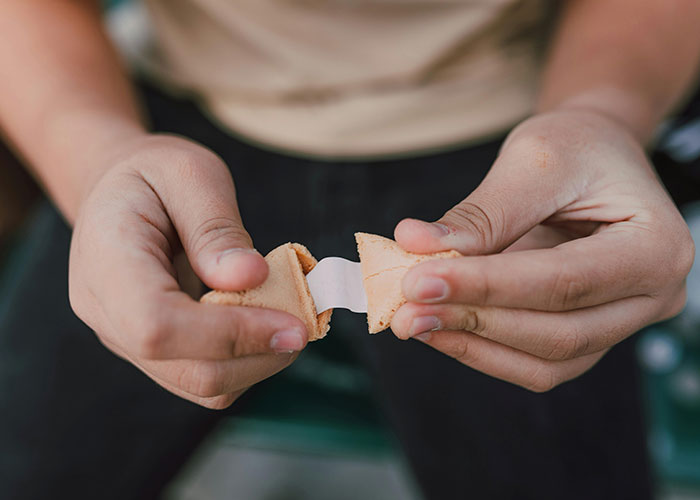 Hands breaking open a fortune cookie revealing a slip of paper, illustrating unlikely events people experienced.