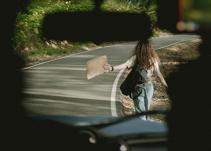 Young woman hitchhiking on a winding road symbolizing unlikely events people experienced in improbable situations