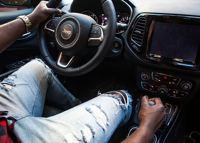 Person driving a Jeep, wearing ripped jeans and a gold watch, experiencing an unlikely event behind the wheel.