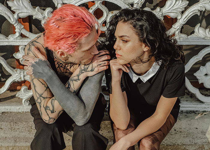 Two young people with tattoos and dyed hair share a close moment reflecting on unlikely events people experienced.