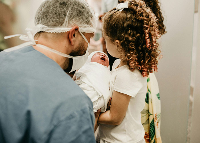 Father in surgical attire and child holding a newborn baby, capturing an unlikely event people experienced moment.