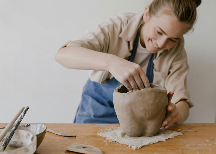 Young woman shaping pottery with clay on table, illustrating improbable but possible creative events experienced.