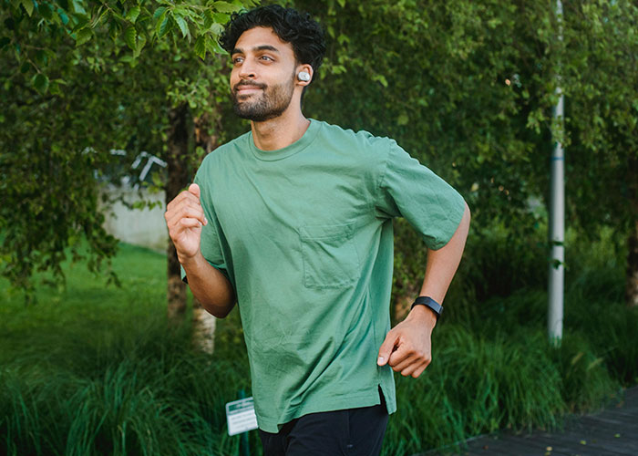 Man jogging outdoors wearing earbuds and a smartwatch, experiencing an unlikely event in a green park setting.