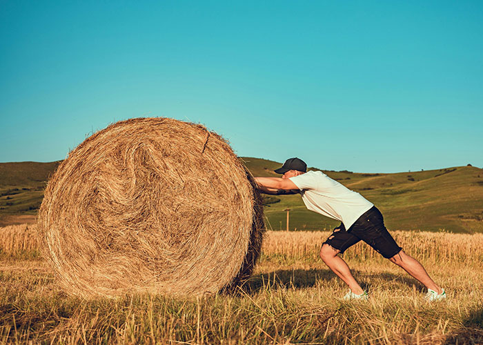 Man pushing large hay bale in open field under clear sky, illustrating improbable yet possible unlikely events experienced.