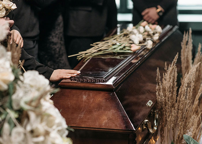 Mourners dressed in black gather around a wooden coffin with flowers, reflecting on improbable unlikely events experienced.