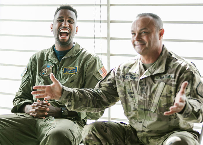Two military personnel laughing and sharing stories about unlikely events people experienced during a casual discussion.