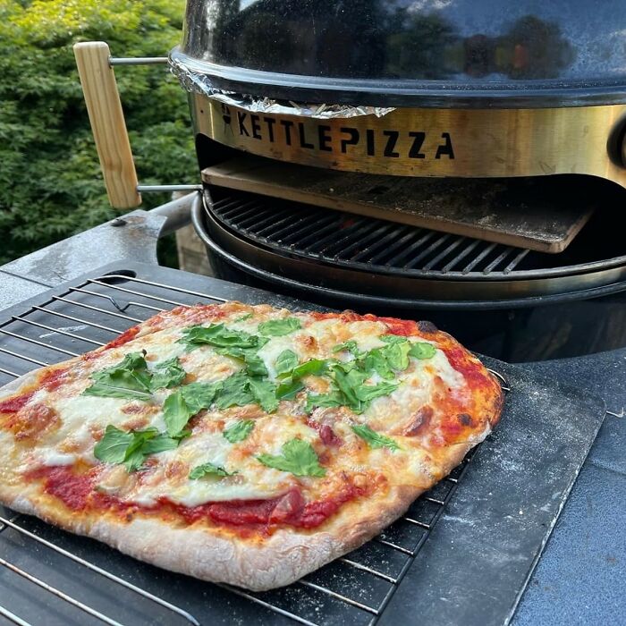 Outdoor kettle pizza oven grilling a fresh pizza with melted cheese and fresh greens for a dopamine hit novelty find.