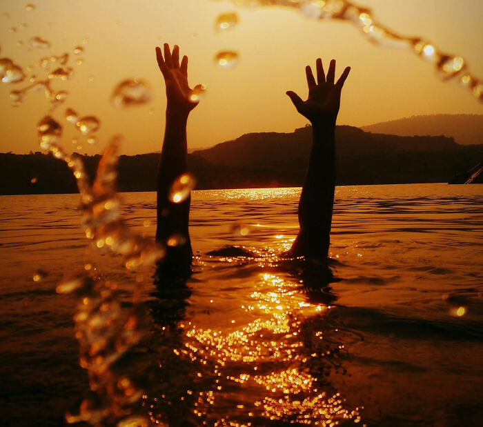 Person raising hands for help in water at sunset, illustrating frightening vacation stories instead of relaxation.