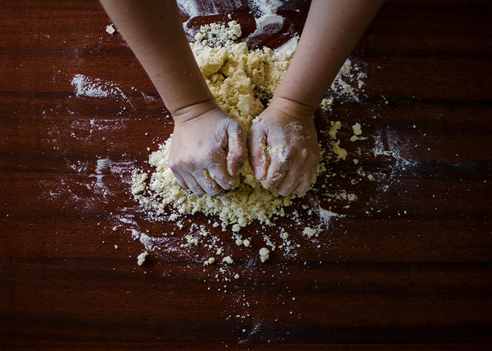 Child’s hands kneading dough on a wooden surface covered in flour, highlighting strange childhood realities and memories.
