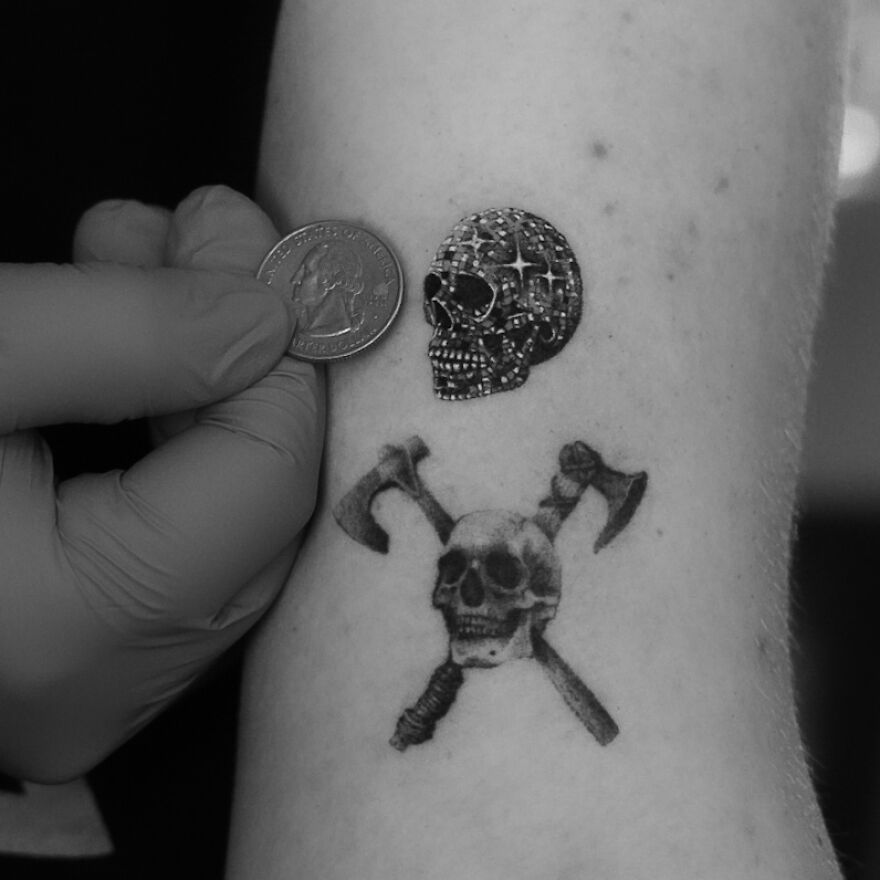 Single needle tattoos of skulls on an arm, with a gloved hand holding a coin for size comparison.