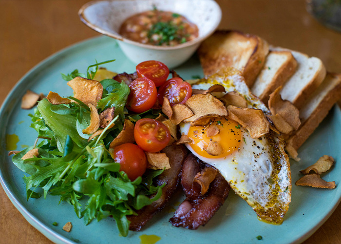 Plate of bacon, fried egg, toast, salad, and tomatoes illustrating everyday things most people don’t realize are deadly.
