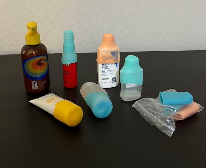 Various travel-size containers and lotion bottles with colorful silicone caps on a black surface, genius Amazon finds concept.