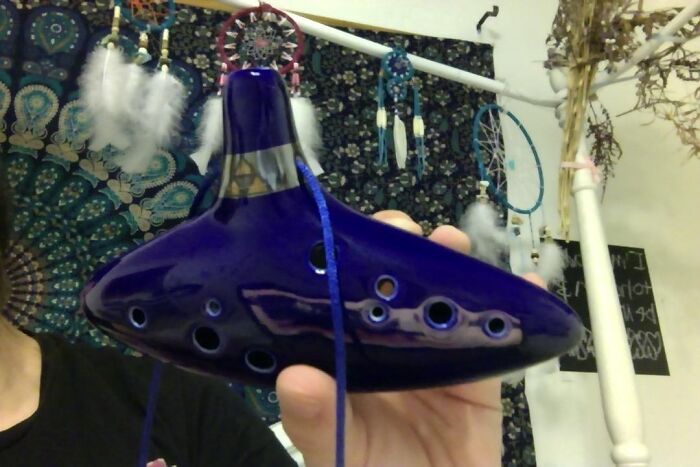 A person holding a shiny blue ocarina with dreamcatchers in the background.
