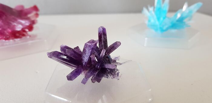 Colorful crystal formations on display; vibrant purple, blue, and pink crystals catching attention on clear stands.