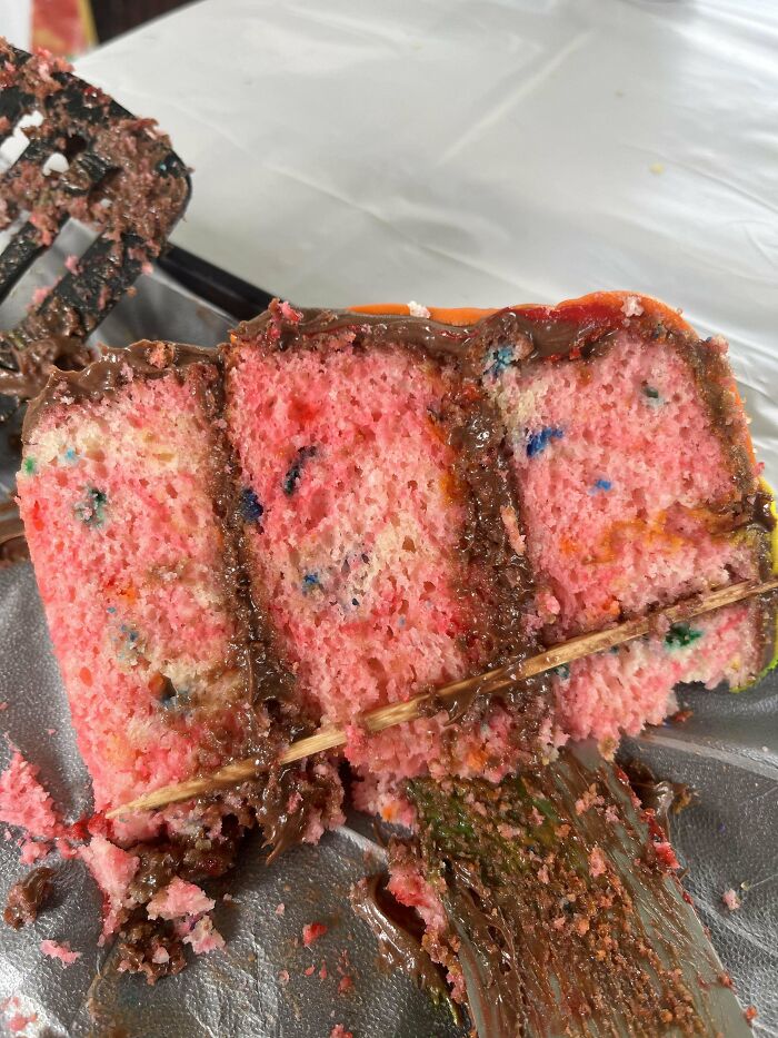 Slice of homemade pink cake with melted chocolate frosting and a skewer stuck through it, showcasing a goofy dad moment.