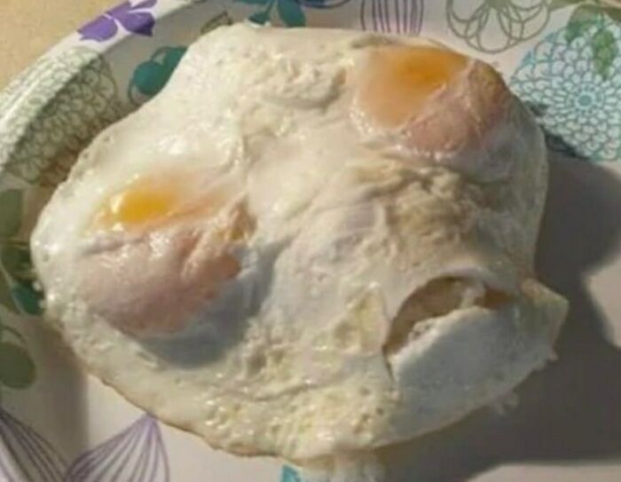 Fried eggs cooked together creating a random and cringe visual on a floral patterned paper plate.