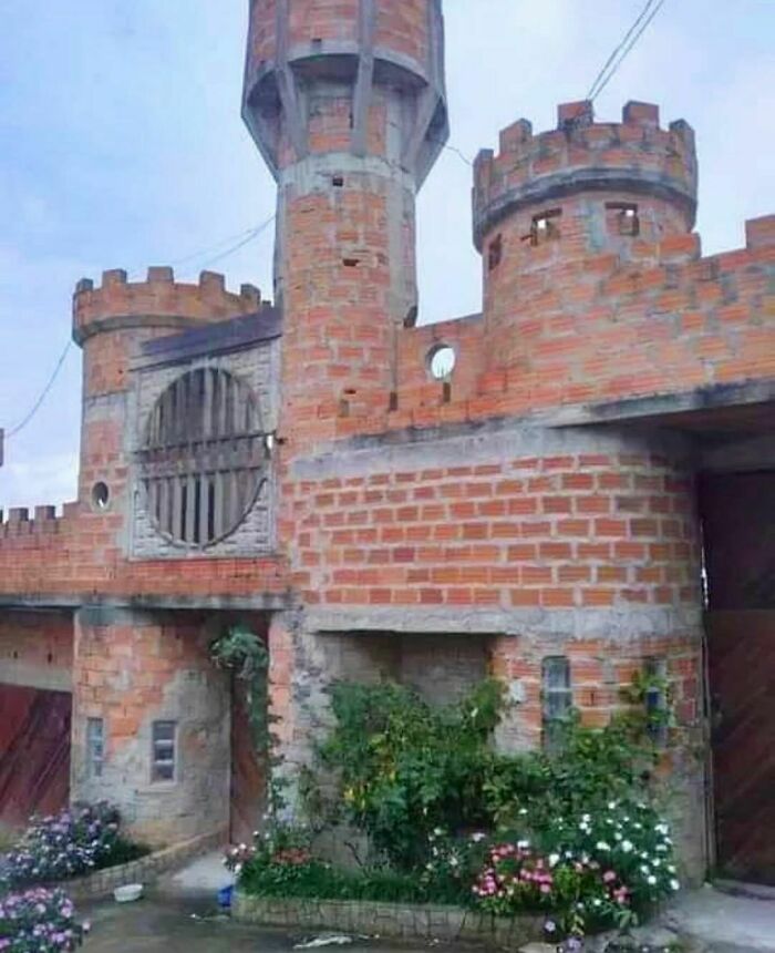 Unfinished brick castle structure with round towers and plants growing near the entrance in a random and cringe photo.