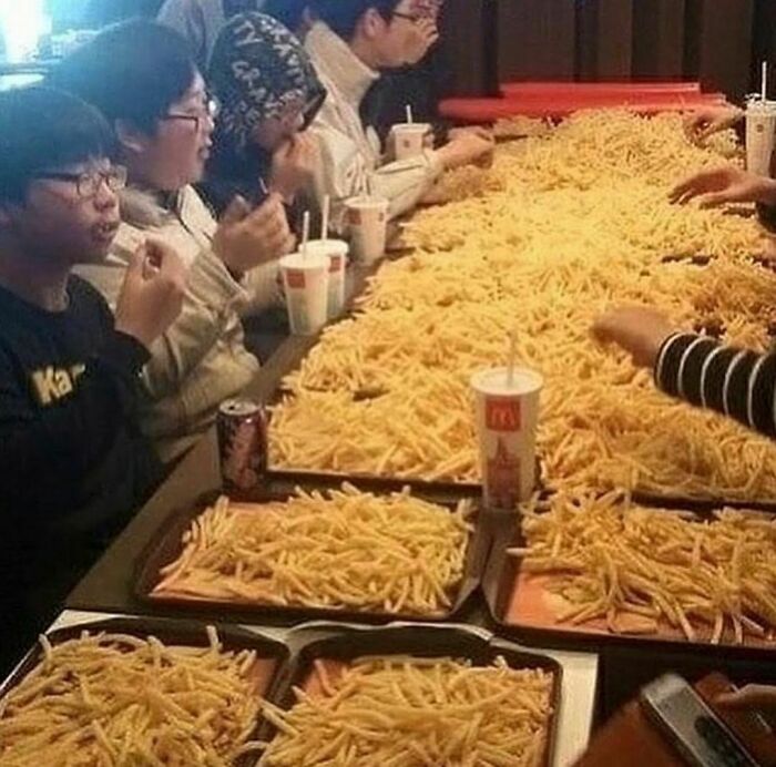 Group of people eating an enormous feast of fries, showcasing random and cringe humor with unique and playful dining style.