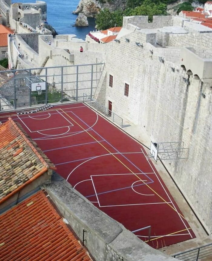 Basketball court uniquely placed along ancient stone fortress walls, blending sports with historic architecture humorously.