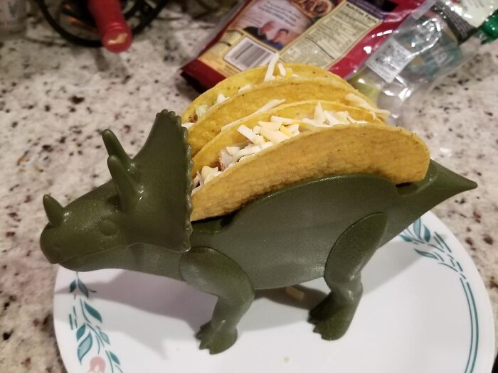 Dinosaur-shaped taco holder with three filled tacos on a kitchen counter.