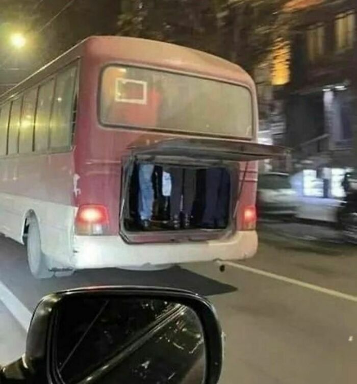 A red bus on the road with its back door open at night.