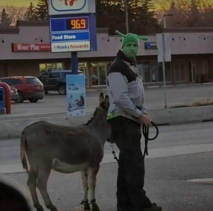 Man dressed as a green ogre with a donkey on a leash in front of a store, capturing a strange Instagram moment.