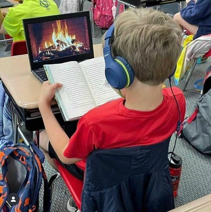 Young boy in class with headphones, reading while a laptop displays a fireplace image. "I Want To Leave Ok" Instagram moment.