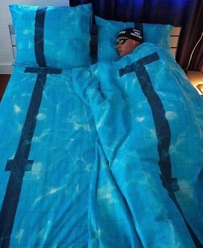 Person dressed as a swimmer in bed, blue sheets resembling a pool, from "I Want To Leave Ok" Instagram account.