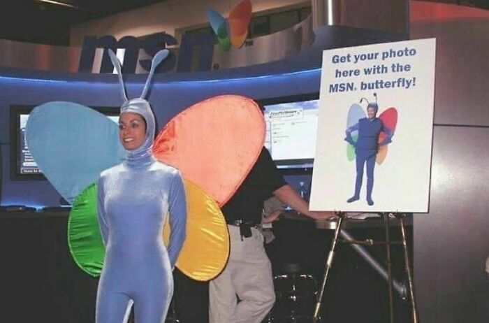 Person in a colorful butterfly costume next to a sign at an event, highlighting a weird Instagram account theme.