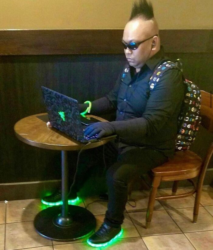 Person with a mohawk and glowing sneakers using a laptop in a cafe.