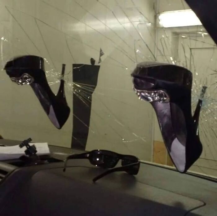 High heels embedded in a shattered car windshield, next to sunglasses. It's as weird as "I Want To Leave Ok" content.