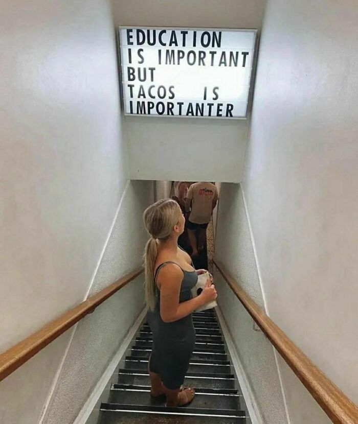 A woman on stairs under a humorous sign about education and tacos from a weird Instagram account.