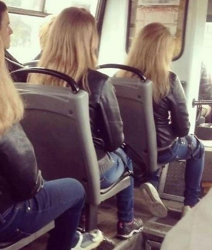 Two women with similar hairstyles and black jackets sitting on a bus, creating a mirrored effect; weird Instagram moment.