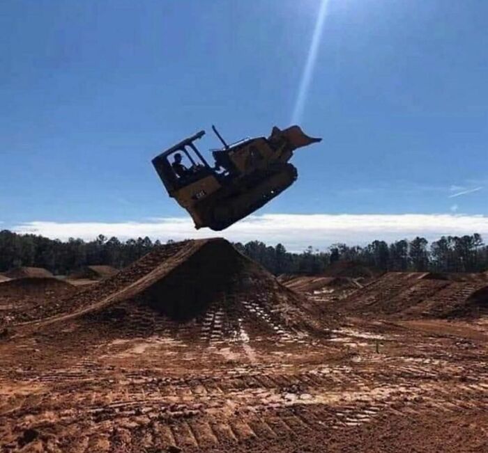 Bulldozer airborne over dirt mound at a construction site creating an awkward photo moment.