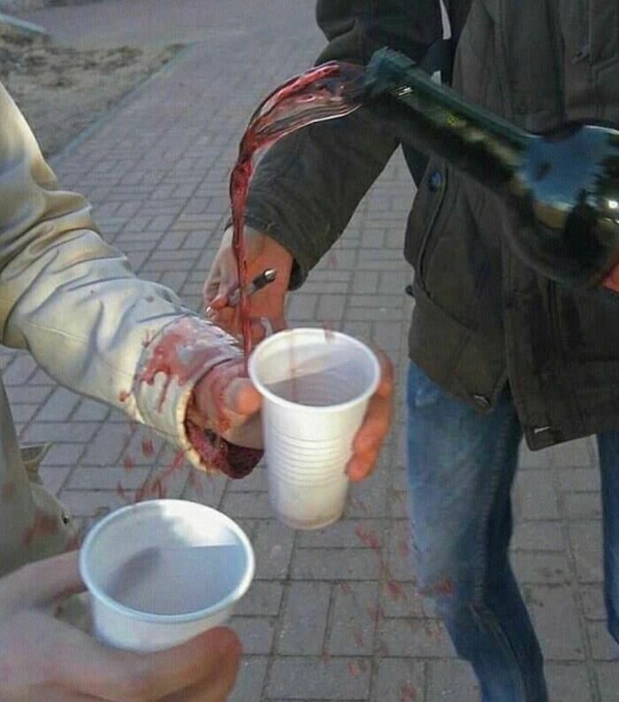 Red liquid spilling on person’s sleeve and pavement while pouring into plastic cup, a painfully awkward photo moment.