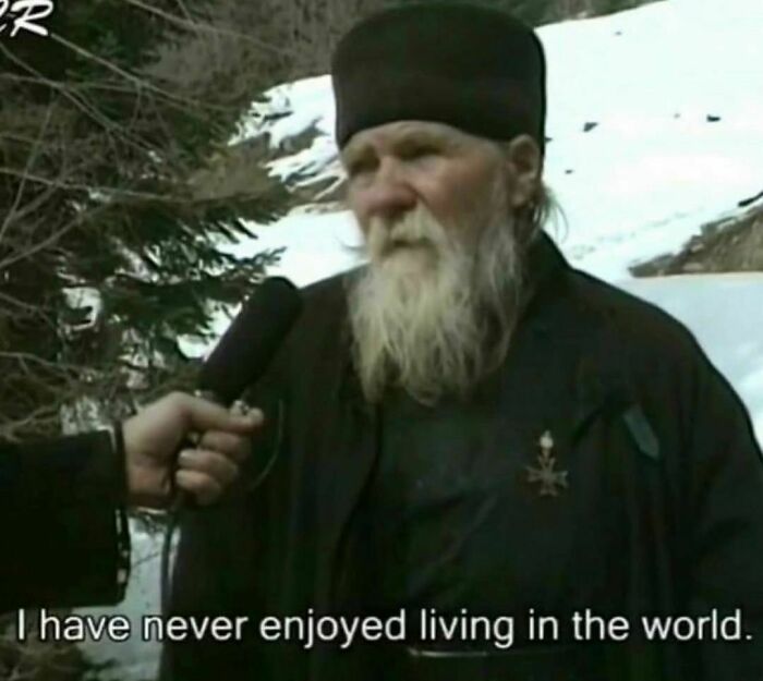 Elderly man with a long beard in awkward photo being interviewed outdoors in a snowy setting with trees nearby.